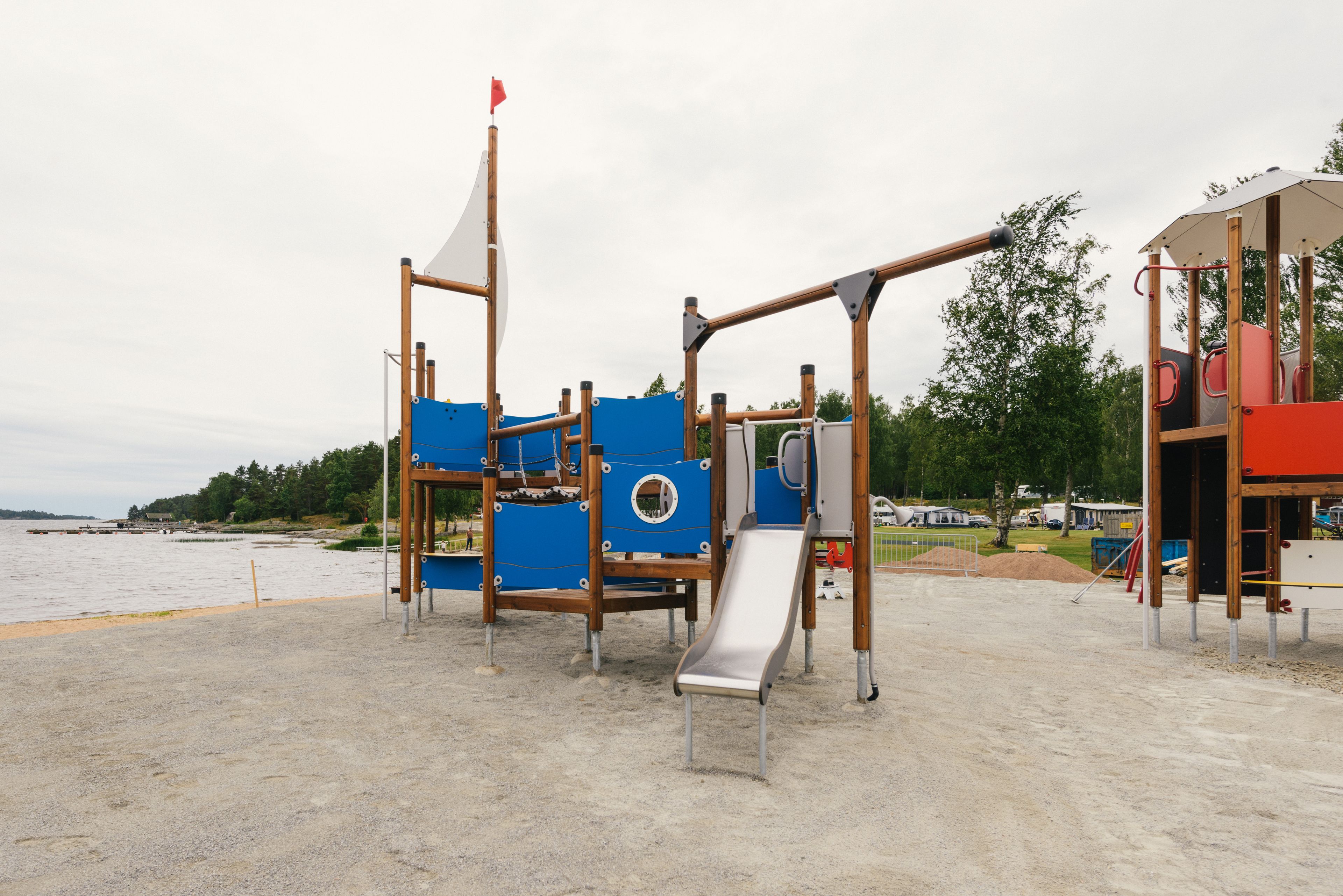 Legeplads med rutsjebane og klatrestrukturer ved vand.