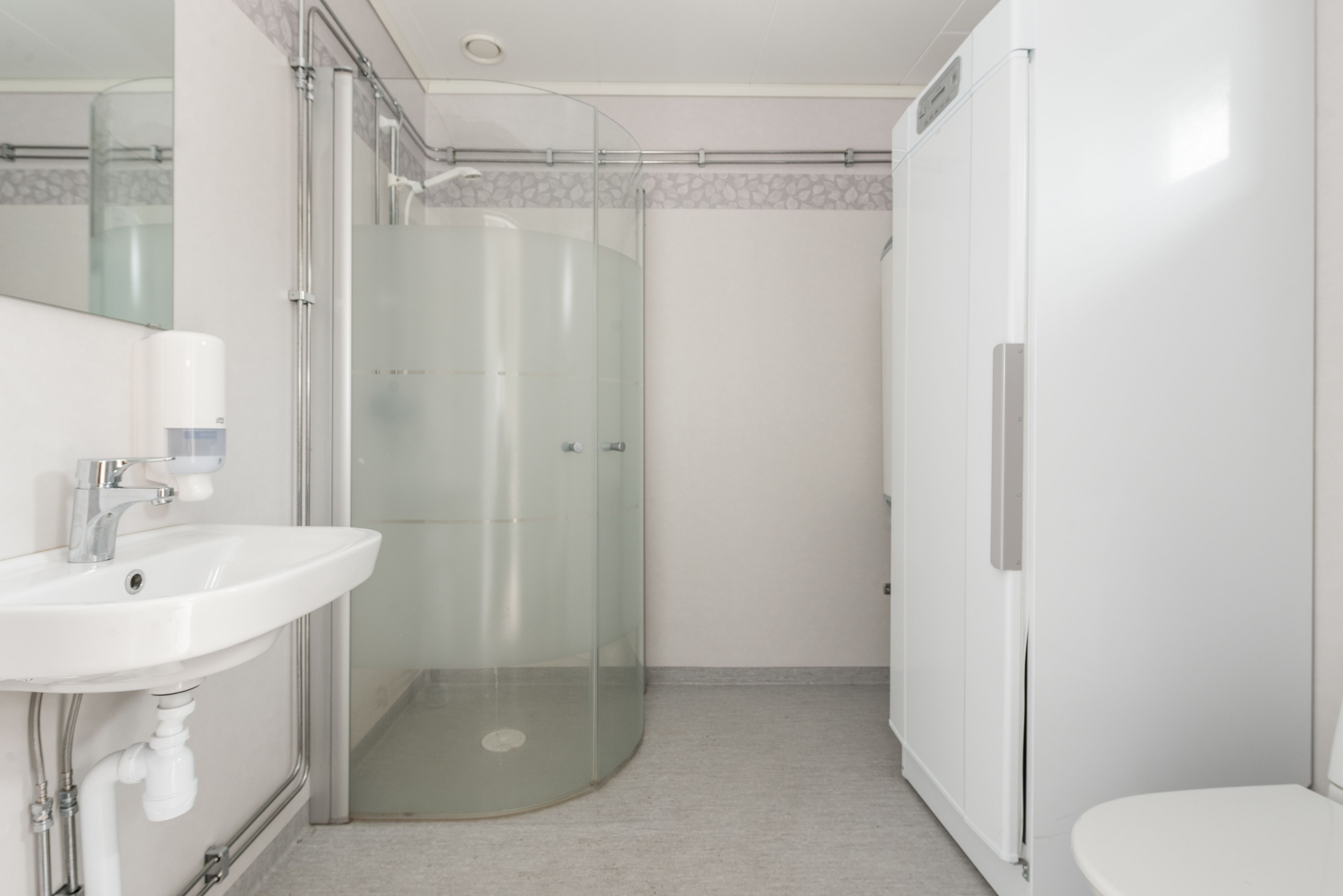 Un baño moderno con ducha envuelta en vidrio, un lavamanos blanco y un inodoro.