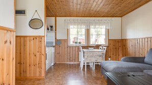 Interior acogedor de una cabaña con paredes y pisos de madera, un comedor con mesa y sillas, y un sofá gris.