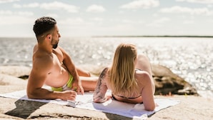 Dos personas sentadas en una toalla de playa cerca del agua.