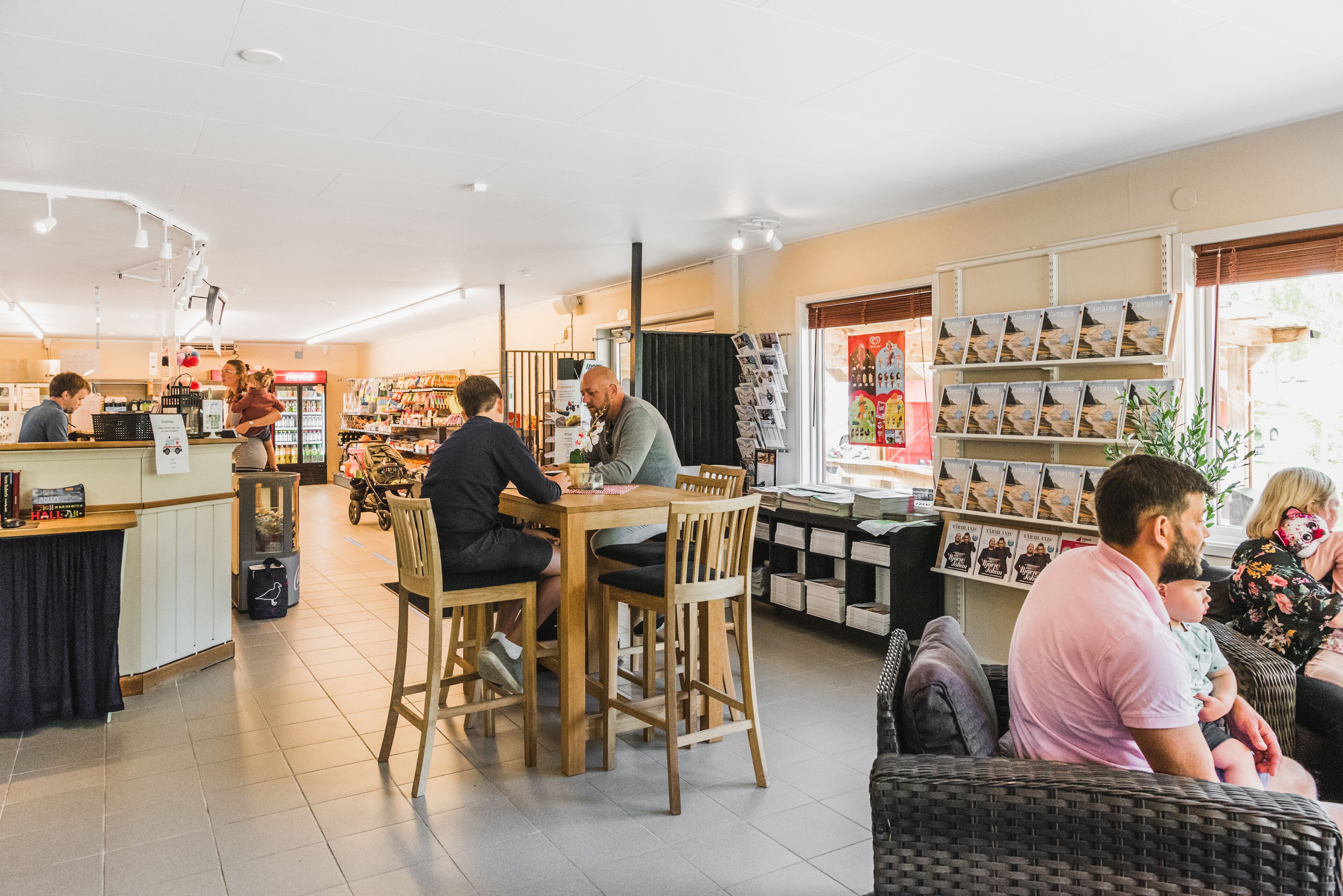 Een boekwinkel met houten tafels en stoelen, een balie en boeken- en tijdschriftenrekken.