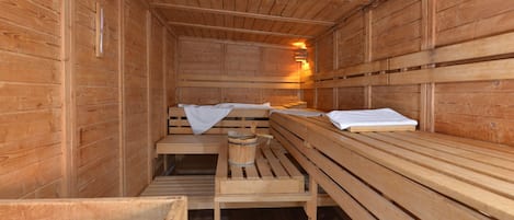 Una sauna con bancos de madera, un banco con un balde y un banco con una toalla.