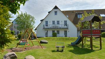 A playground with swings, a slide, and a climbing structure in front of a two-story house with a balcony.