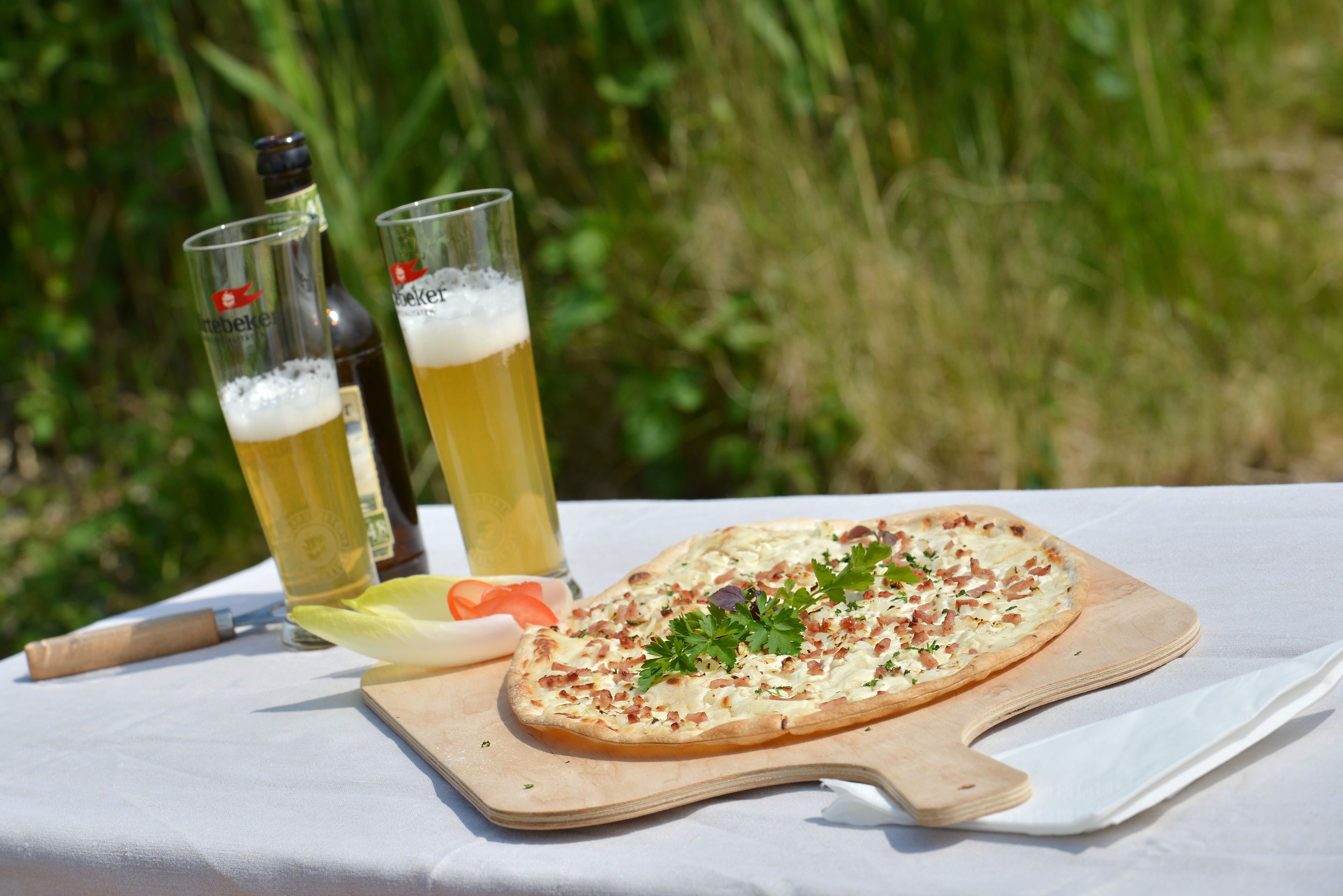 Una pizza su un tagliere di legno, con un coltello e due bicchieri di birra su un tavolo all'aperto.