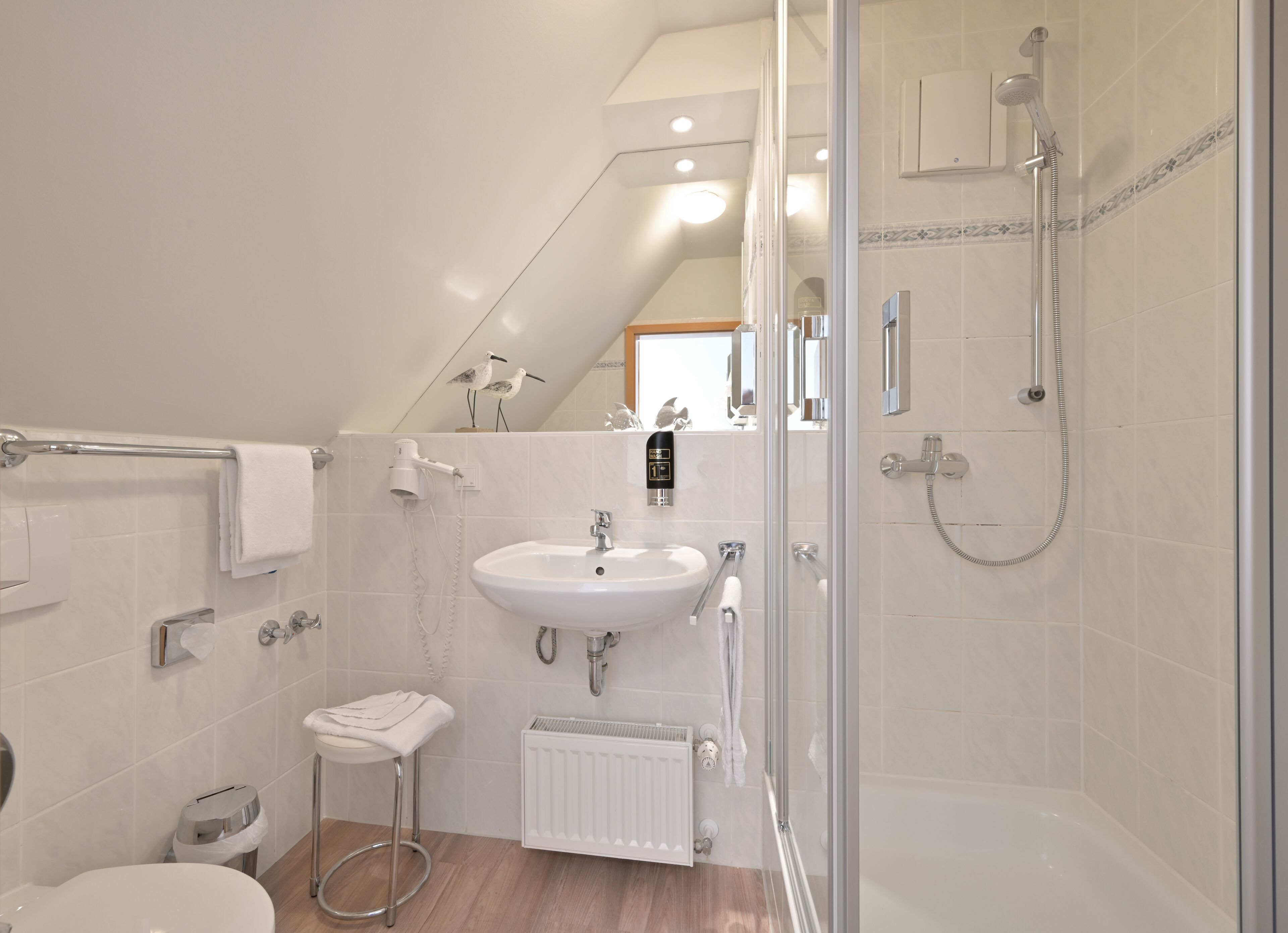 Un baño moderno con cabina de ducha de vidrio, un lavabo blanco y un taburete pequeño.