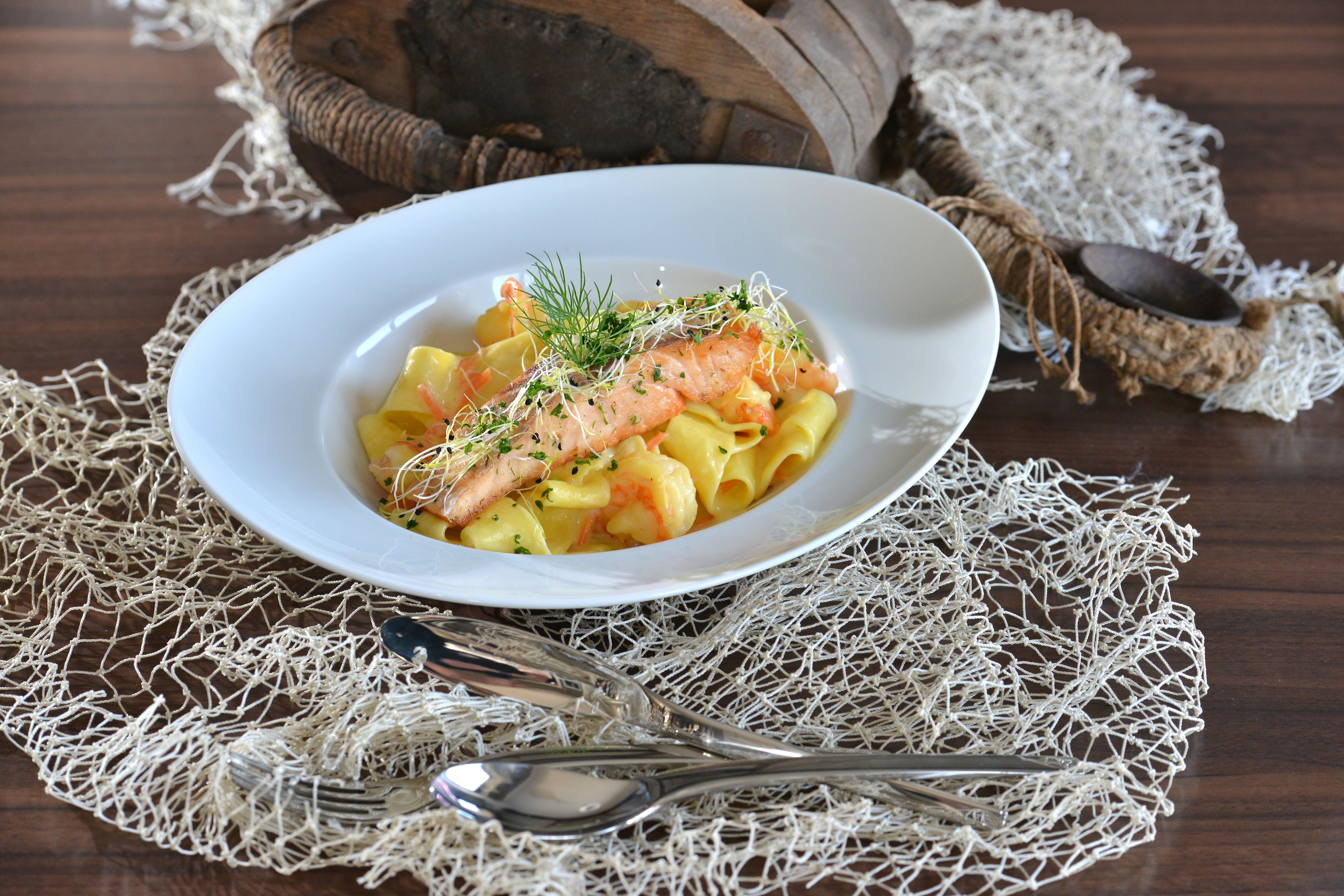 Een bord pasta met zalm en garnering, geplaatst op een kanttafelkleed.
