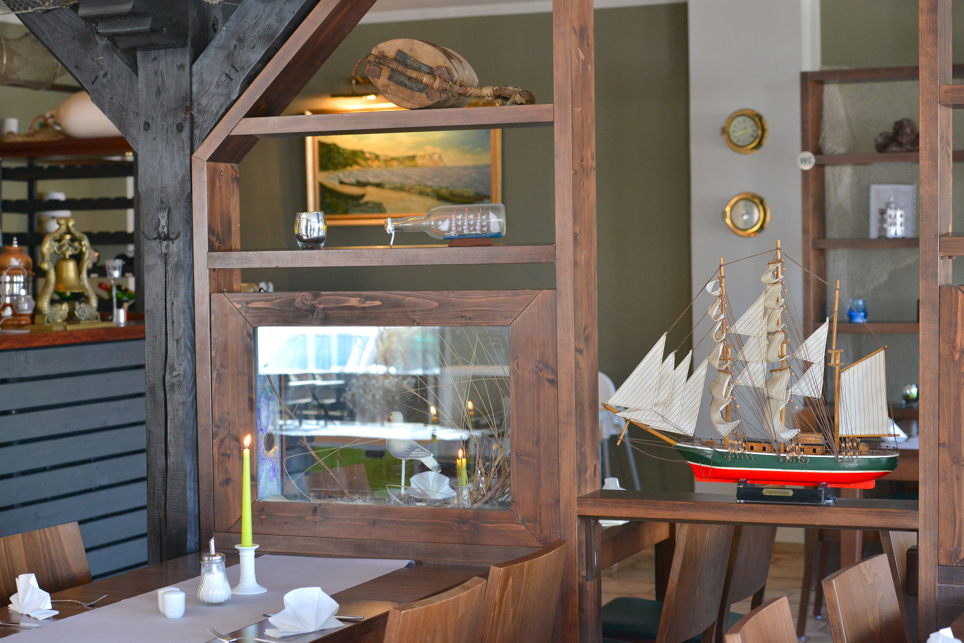 Un comedor con una mesa de madera, sillas, velas y un barco modelo en un estante.