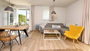 A modern living room with a wooden dining table, wicker chairs, a yellow armchair, a white sofa, and a coffee table. - Kapitäns-Häuser Breege (Breege)