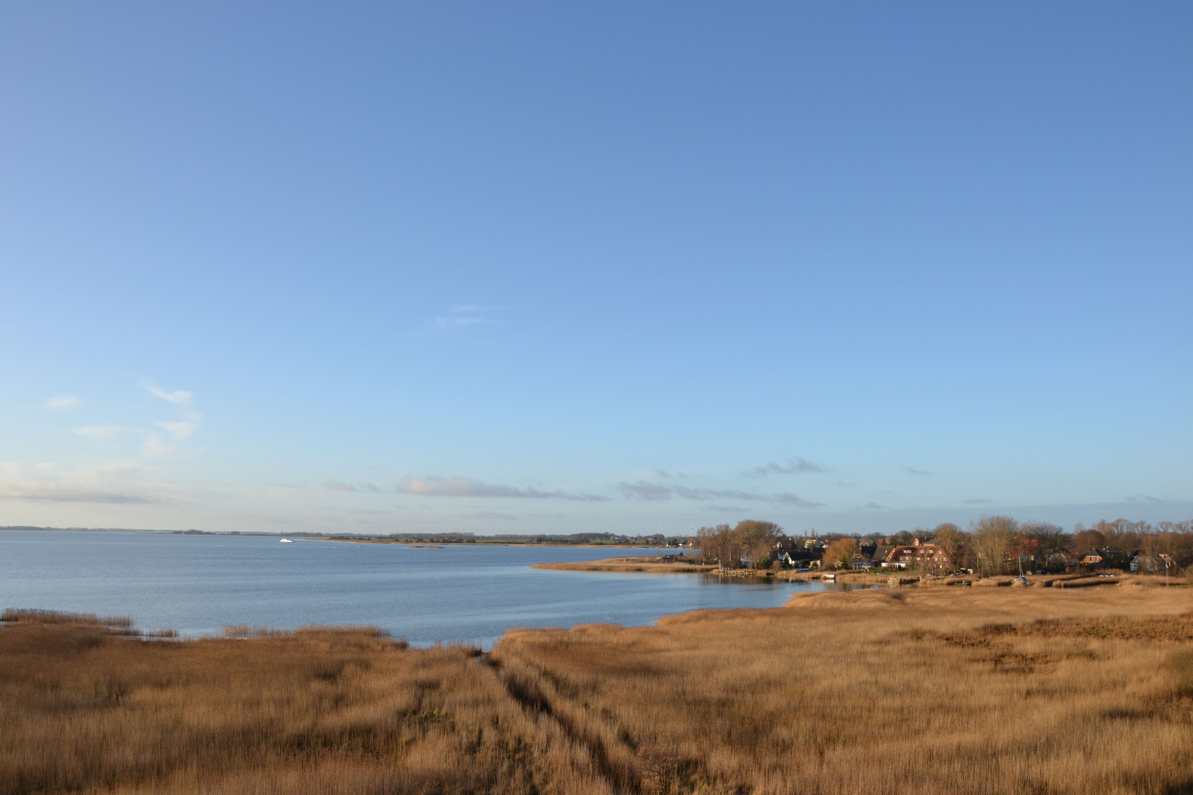 A coastal landscape with a clear sky, a body of water, and a few buildings in the distance.