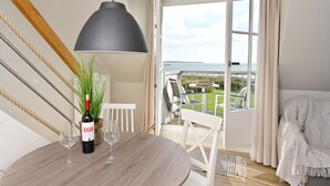 A room with a wooden table, a wine bottle, and glasses, a hanging pendant light, and a view of a balcony with outdoor seating and a body of water. - Kapitäns-Häuser Breege (Breege)