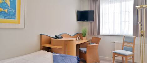 A hotel room with a bed, a desk with a chair, a television, and a window with curtains.