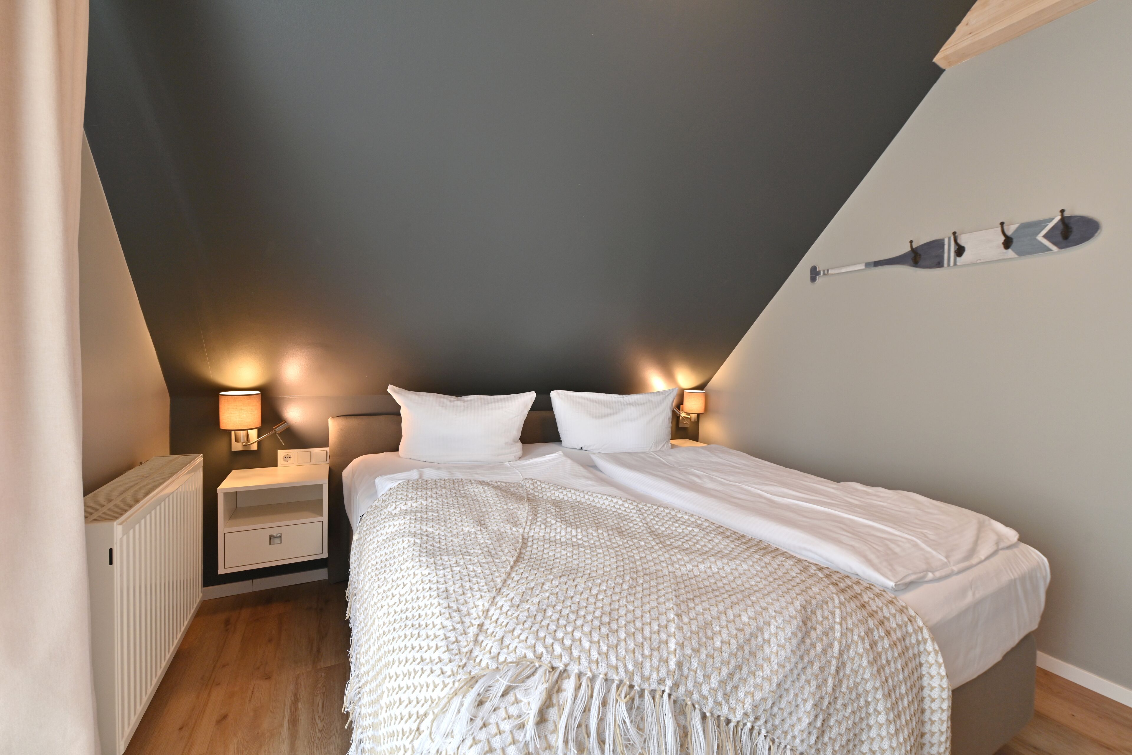 A bedroom with a bed, bedside tables, and a wall-mounted light fixture.