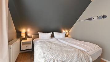 A bedroom with a bed, bedside tables, and a wall-mounted light fixture.