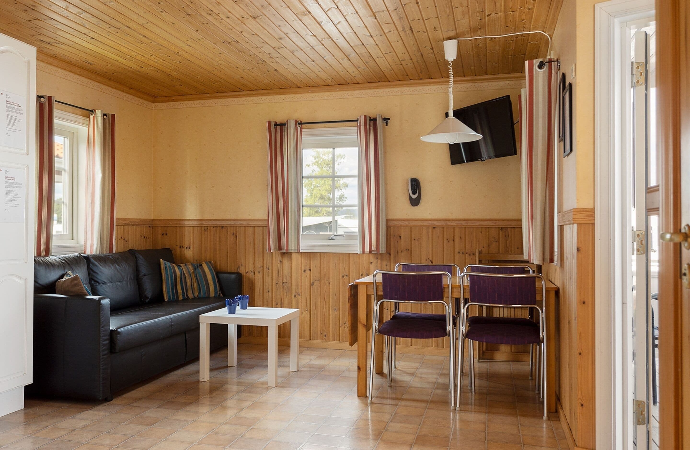Una habitación acogedora con techo de madera, un sofá de cuero negro, una mesita blanca pequeña y dos sillas moradas.