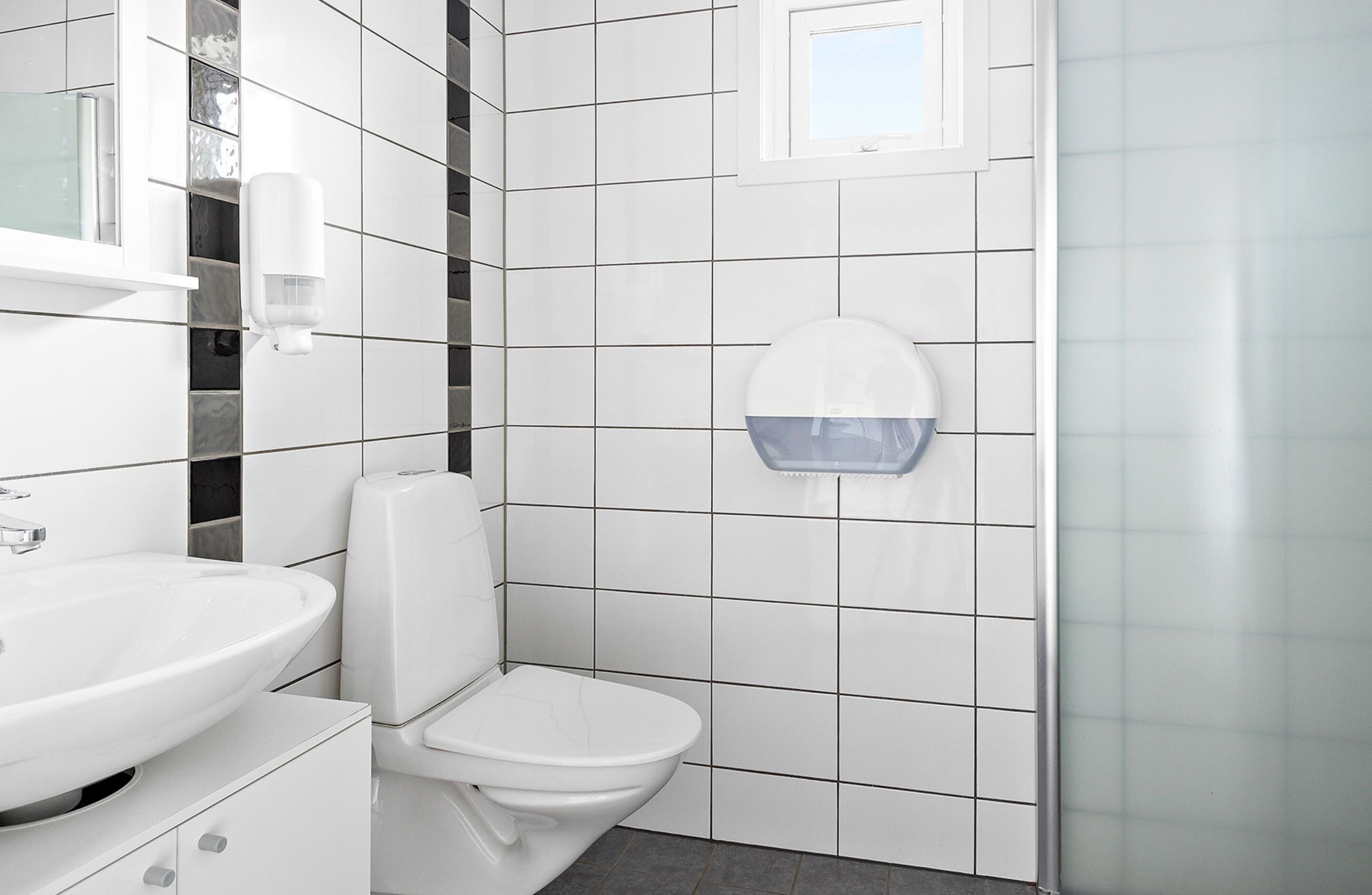 Ein modernes Badezimmer mit einem weißen Waschbecken, einer Toilette und einem an der Wand befestigten Handdesinfektionsmittelspender.