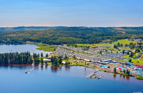 Vista aérea de un resort junto al lago, con un puerto deportivo, un amplio estacionamiento y diversos edificios, incluyendo un hotel y espacios de recreación.