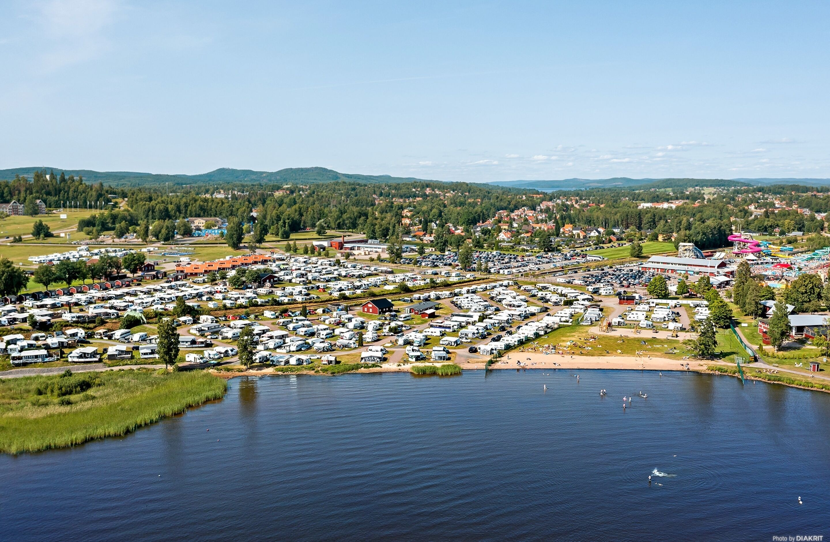 A large RV park with numerous vehicles and a lake in the foreground.