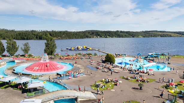 A water park with multiple pools and slides, surrounded by a lake and forested hills. - First Camp Sunne (Sunne)
