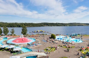 Parque acuático con múltiples piscinas y toboganes, rodeado por un lago y colinas boscosas.