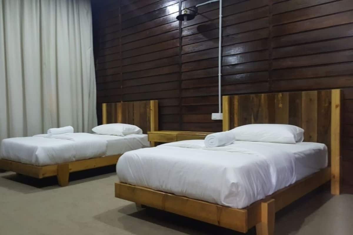 Dos camas de madera con sábanas blancas en una habitación con paneles de madera en las paredes.