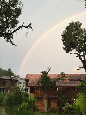 A house with a red-tiled roof, surrounded by lush greenery and a visible rainbow in the sky.