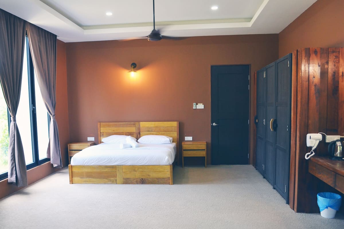 Un dormitorio con cama, mesita de noche, escritorio con teléfono y hervidor, armario y ventana con cortinas.