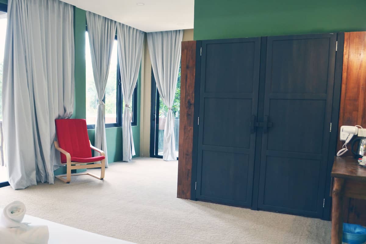 Una habitación de hotel con un amplio armario de madera, una silla roja y una cama con una toalla blanca.
