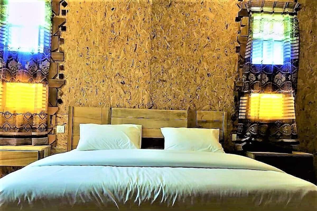 Una cama con cabecera de madera, dos almohadas y una mesita de noche con lámpara.