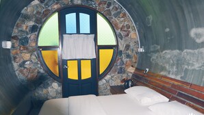 A bedroom with a stone wall, a circular window, and a wooden headboard. - The Acacia Retreat (Bentong)