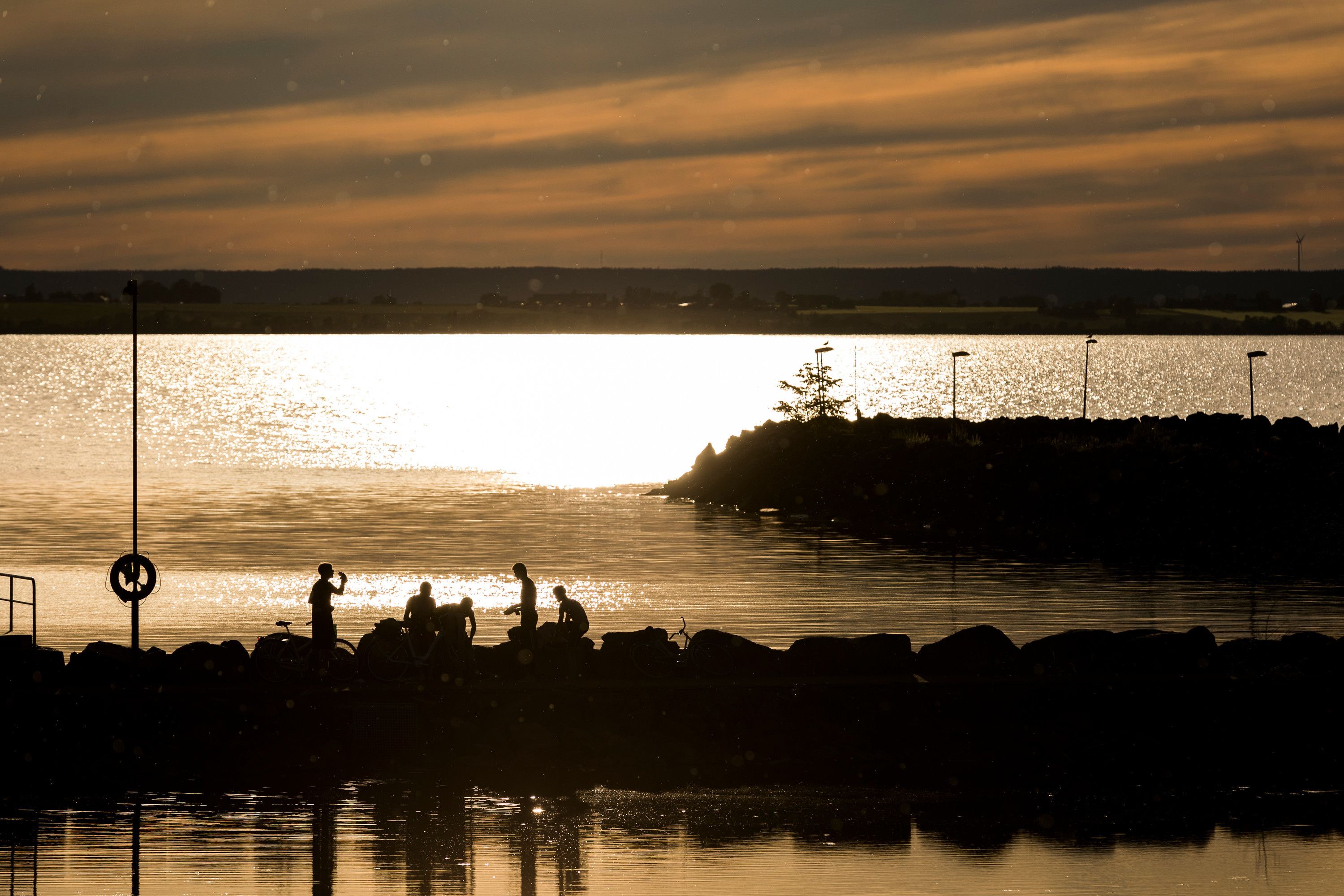 Um pôr do sol sobre águas calmas, com silhuetas de pessoas e uma bicicleta.