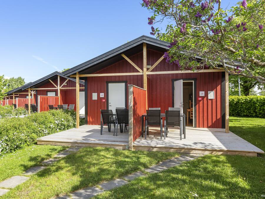 Filas de cabañas de madera roja con asientos exteriores y un jardín.