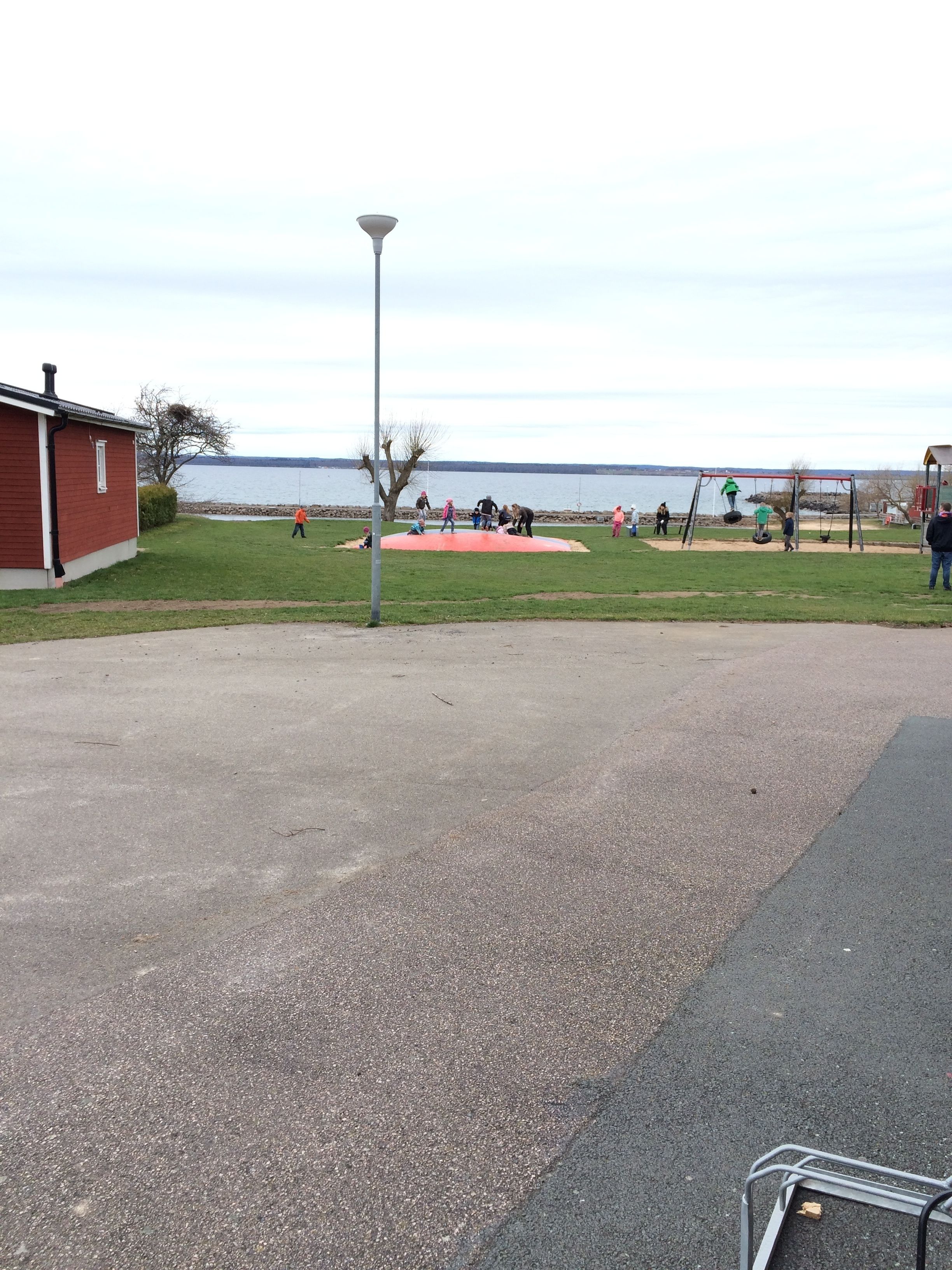A park with a playground, a red building, and a body of water in the background.