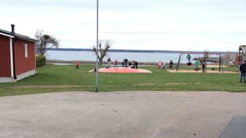 A park with a playground, a red building, and a body of water in the background.