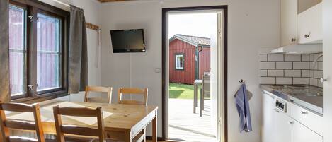 Una cocina con techo de madera, un comedor con mesa y sillas, un televisor montado en la pared y vista a un edificio rojo en el exterior.