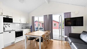 Una cocina moderna con armarios blancos, una mesa de comedor con sillas, un sofá y un televisor montado en la pared.