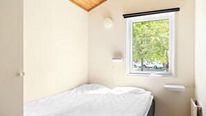 Una habitación pequeña con cama individual, ventana a la calle, radiador e iluminación en el techo.