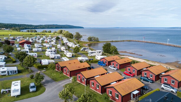 Un camping con vehículos recreativos y casas móviles, un cuerpo de agua y un muelle.