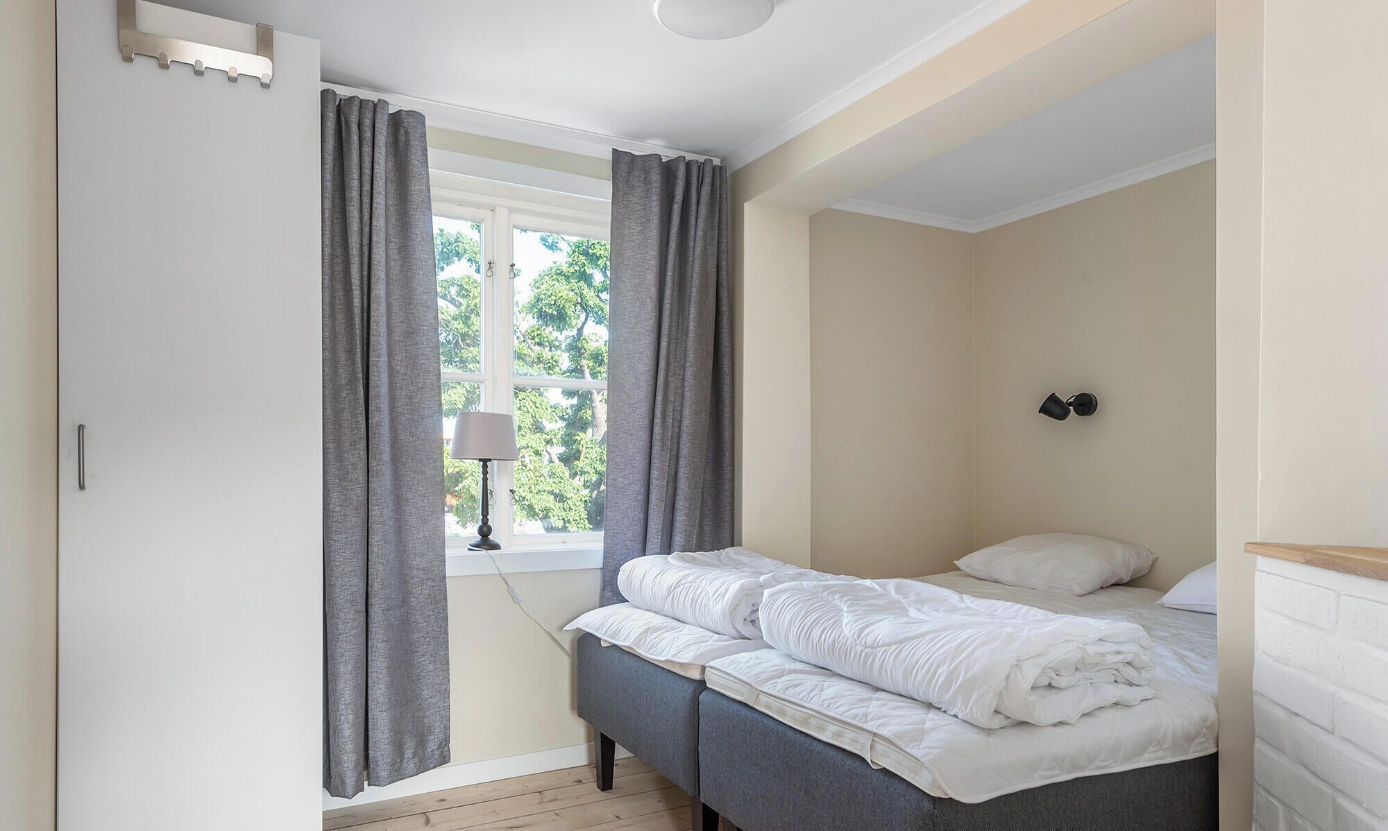 Een slaapkamer met een bed, gordijnen, een lamp en een raam.