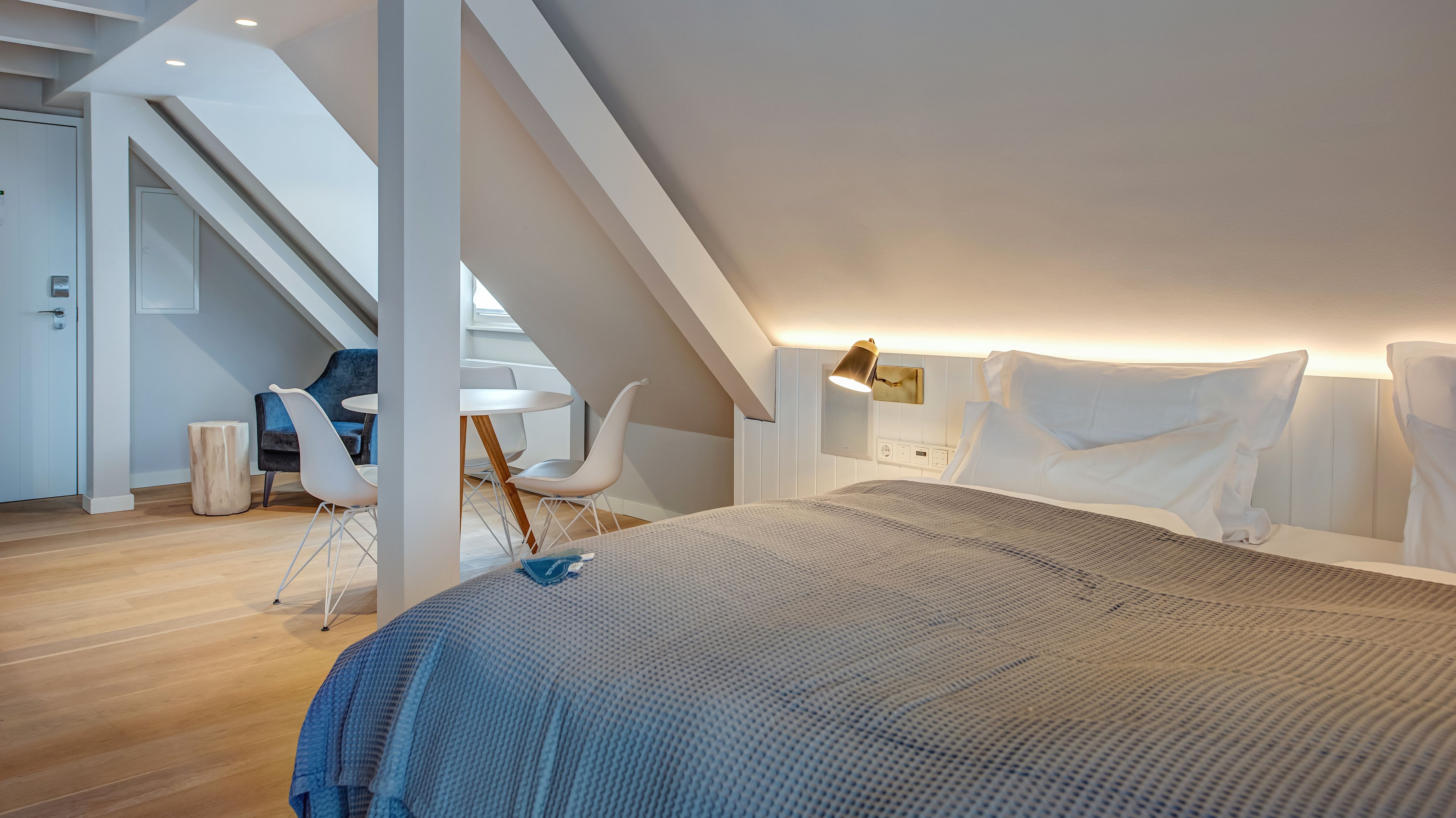 Un dormitorio moderno con techo inclinado, una cama grande, un escritorio y una silla.
