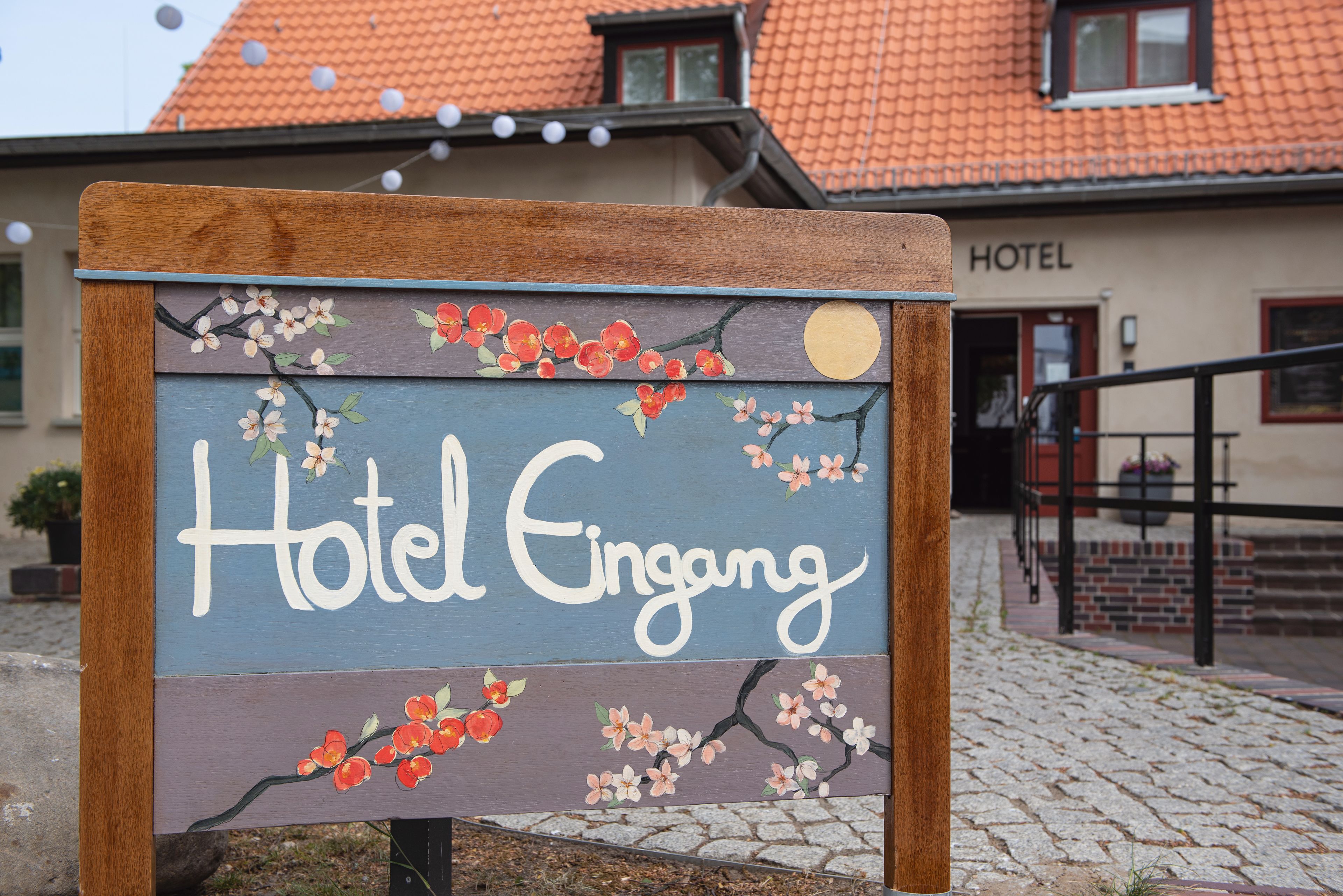 Un letrero de madera con la inscripción 'Hotel Eingang', decorado con motivos florales y una luna.