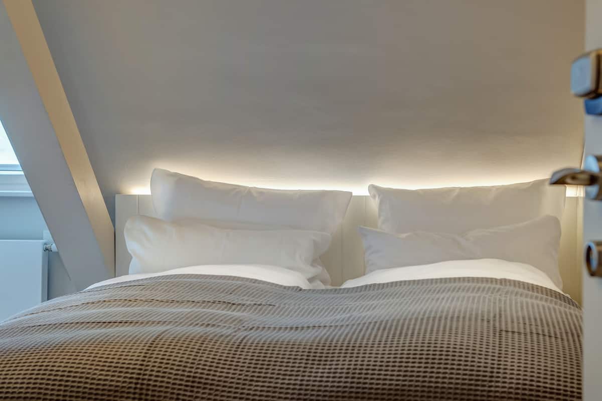 A modern bedroom with a large bed, white bedding, and a wall-mounted light fixture.