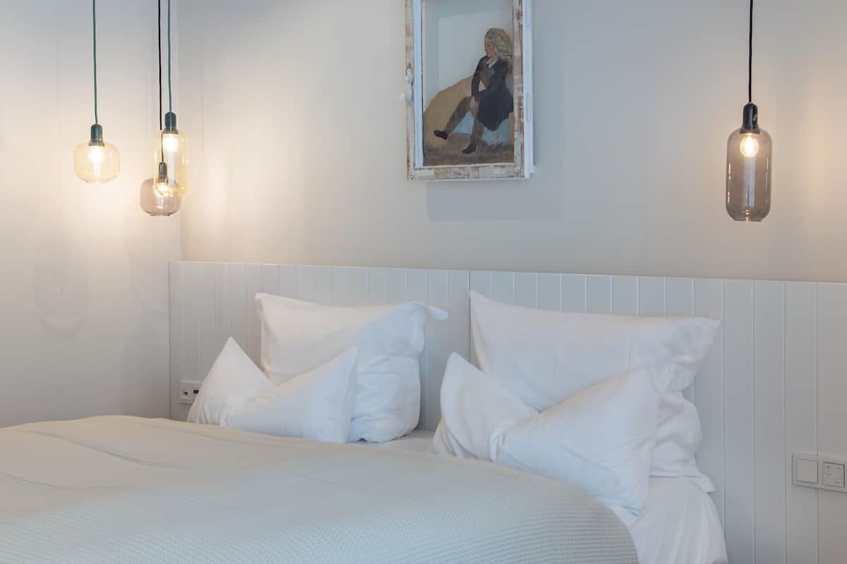A hotel room with a large bed, white bedding, and three hanging pendant lights.