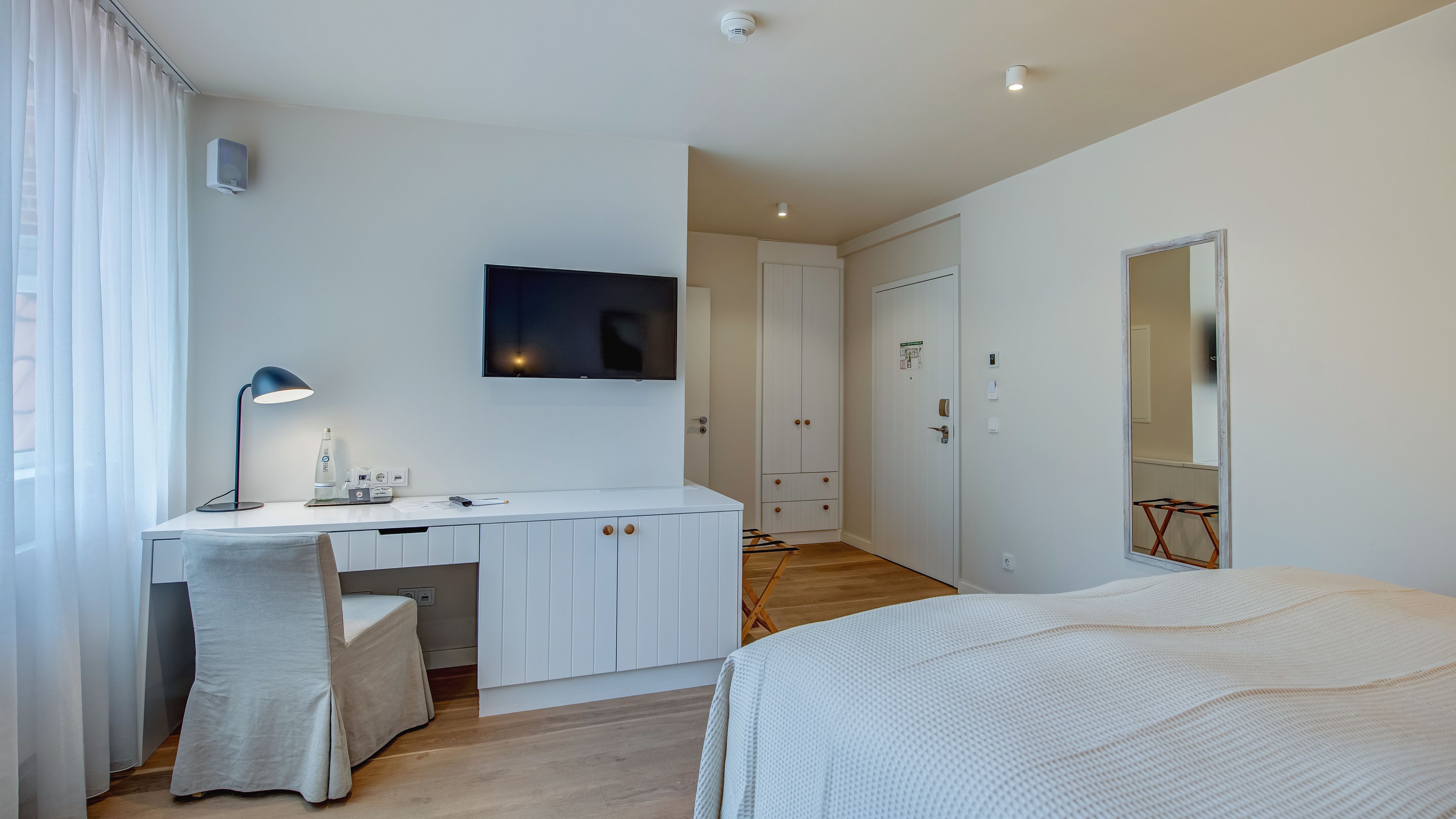 A modern bedroom with a white desk, a bed, a TV, and a wardrobe.