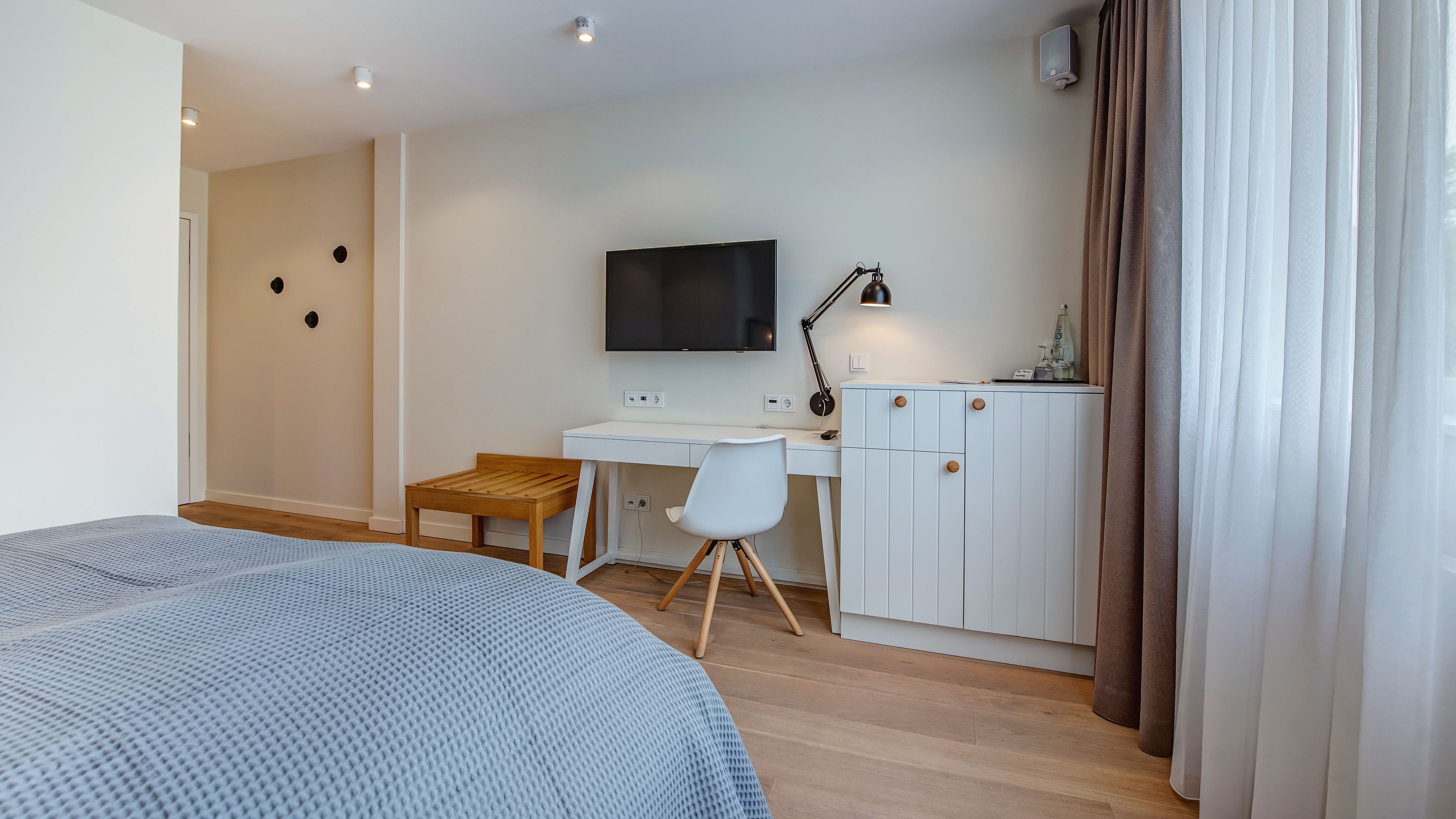A modern bedroom with a bed, a desk, a chair, a TV, and a wardrobe.