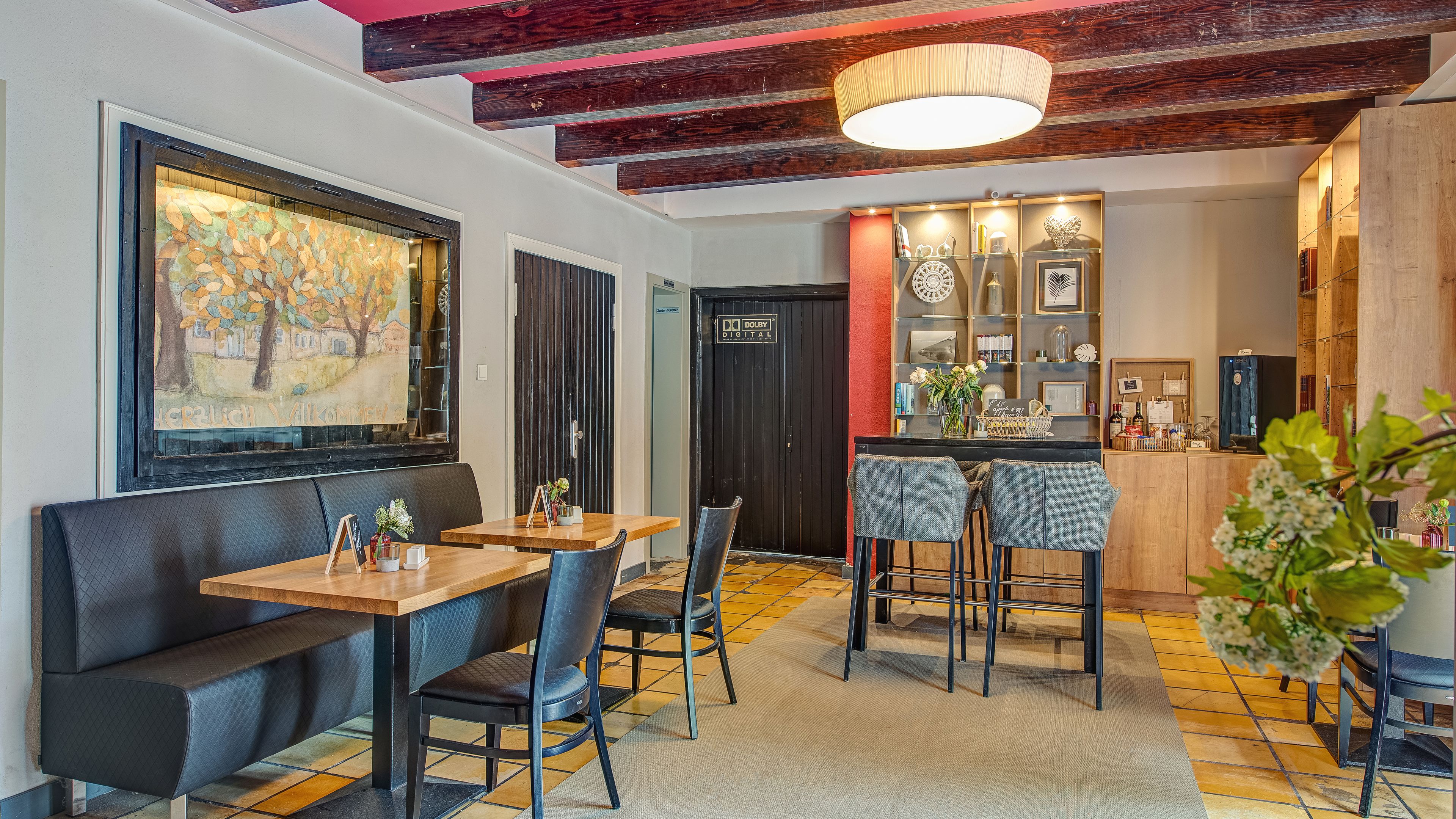 A restaurant with a bar area, wooden ceiling beams, and a large painting on the wall.