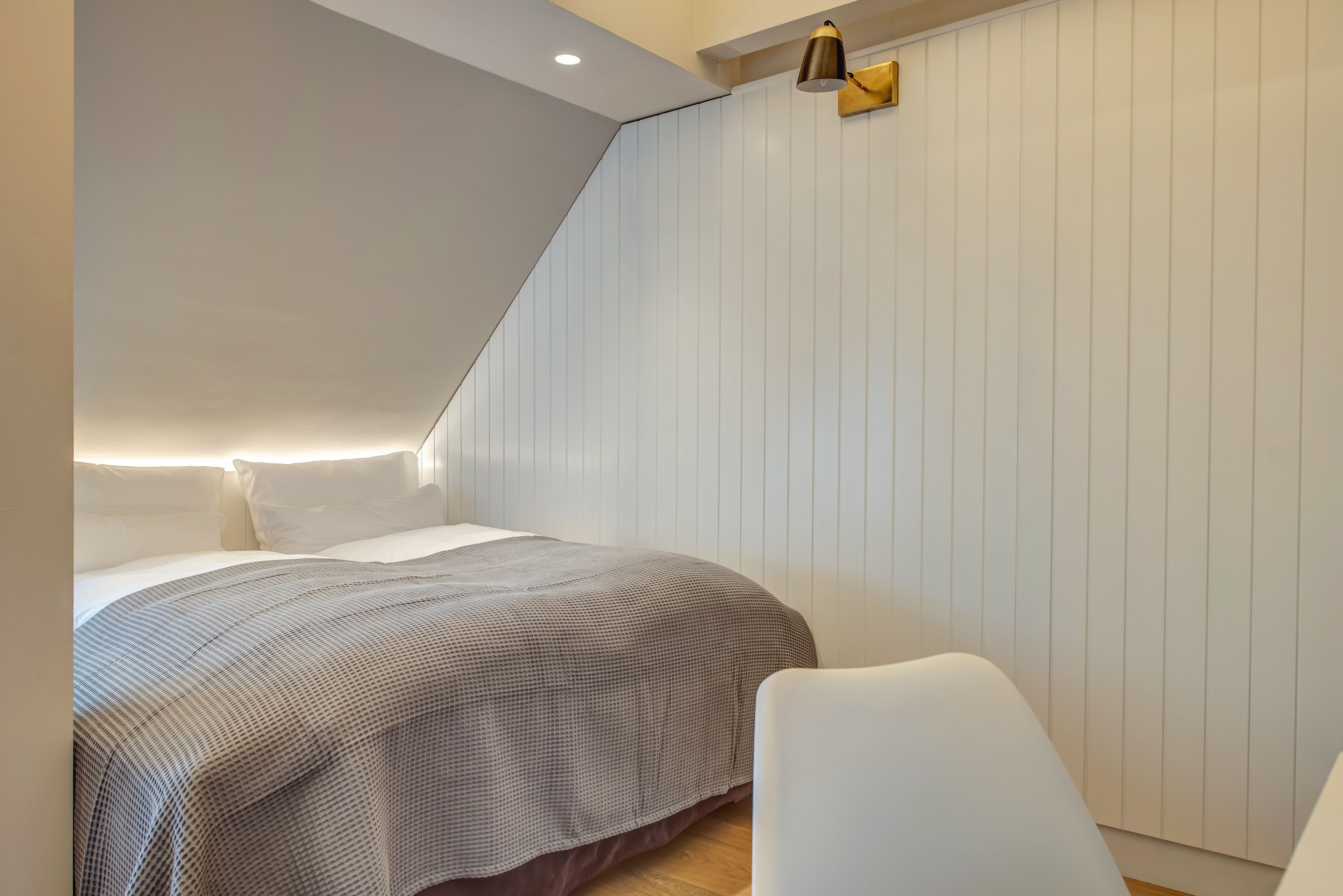 Un dormitorio con una cama, una silla y techo inclinado.