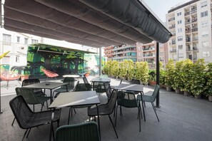 An outdoor seating area with tables and chairs, surrounded by potted plants and a building in the background. - No Limit Hostel Graffiti (Barcelona)