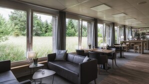 Un comedor moderno con una mesa larga, sillas y un sofá. Ventanas amplias ofrecen vistas a un área con césped.