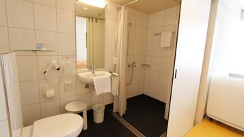 Une petite salle de bain propre, équipée de toilettes, d’un lavabo et d’une douche.