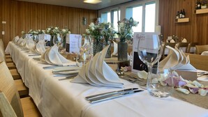 Una larga mesa de comedor con manteles blancos, cubiertos y copas de vino, adornada con arreglos florales y menús sobre la mesa.